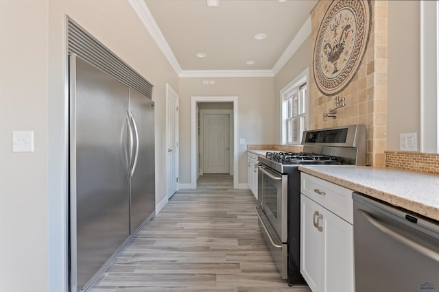 kitchen with high quality appliances, tasteful backsplash, light wood-type flooring, and white cabinetry