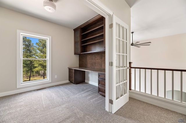 unfurnished office featuring a healthy amount of sunlight, light carpet, ceiling fan, and built in desk