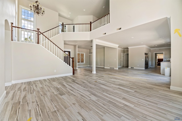 unfurnished living room with a towering ceiling, crown molding, and light hardwood / wood-style flooring