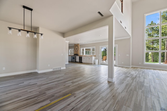 unfurnished living room featuring a wealth of natural light, ornamental molding, and light hardwood / wood-style flooring