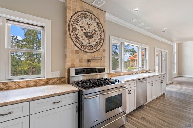 kitchen featuring crown molding, light wood-type flooring, light stone counters, white cabinets, and appliances with stainless steel finishes