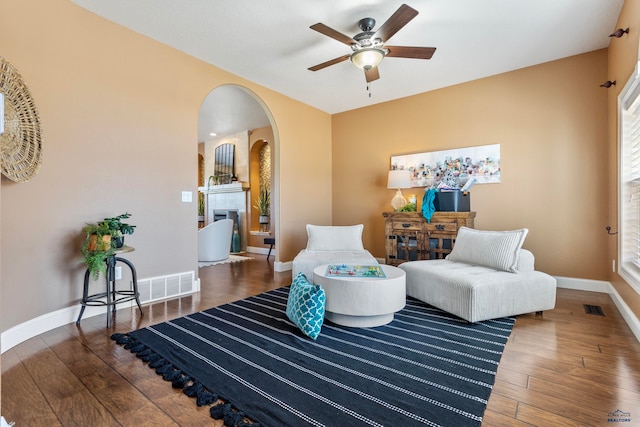 living room with ceiling fan, a fireplace, and dark wood-type flooring