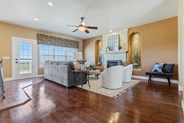 living room featuring ceiling fan, a tile fireplace, and dark wood-type flooring