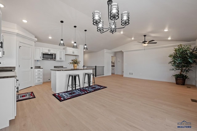 kitchen with white cabinetry, a center island, decorative light fixtures, vaulted ceiling, and a breakfast bar area