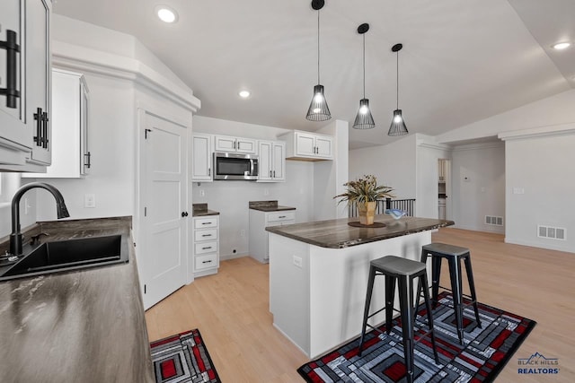 kitchen with white cabinets, lofted ceiling, light hardwood / wood-style floors, a breakfast bar, and sink