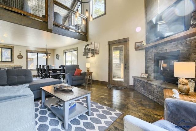 living room with a towering ceiling, a stone fireplace, a chandelier, and dark wood-type flooring