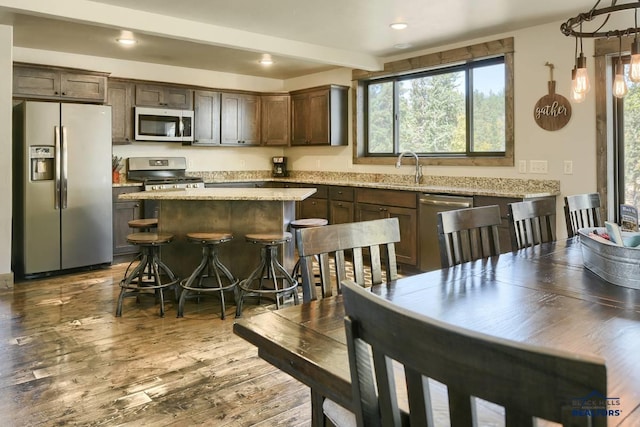 kitchen featuring appliances with stainless steel finishes, a center island, a breakfast bar, pendant lighting, and dark brown cabinetry