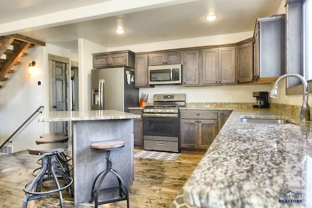 kitchen with sink, a center island, dark hardwood / wood-style floors, light stone countertops, and appliances with stainless steel finishes