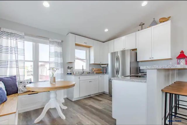 kitchen with a breakfast bar, sink, light hardwood / wood-style floors, light stone counters, and white cabinetry