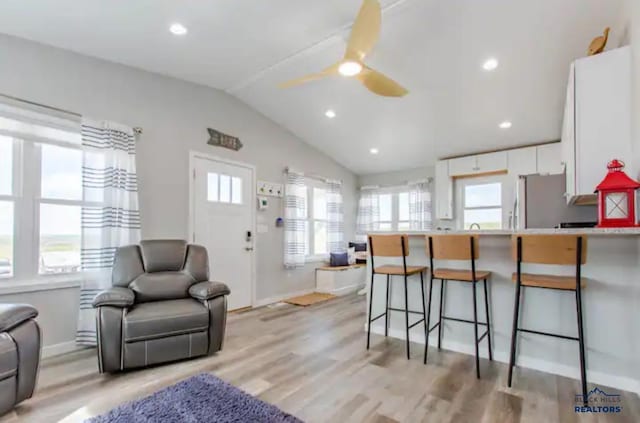 kitchen with stainless steel refrigerator, white cabinetry, ceiling fan, kitchen peninsula, and a breakfast bar area