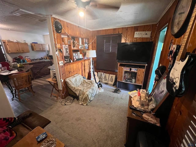 carpeted living room with a textured ceiling, wood walls, crown molding, and ceiling fan