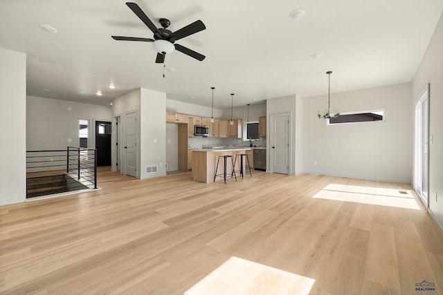 unfurnished living room featuring ceiling fan with notable chandelier, sink, and light wood-type flooring