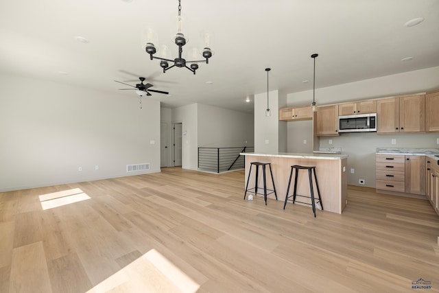 kitchen with hanging light fixtures, ceiling fan with notable chandelier, a kitchen island, a breakfast bar, and light hardwood / wood-style flooring