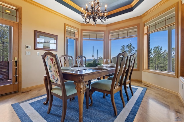 dining area with crown molding, a tray ceiling, light wood-type flooring, and a notable chandelier