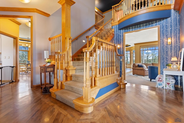 stairs with a notable chandelier, a towering ceiling, ornamental molding, and hardwood / wood-style flooring