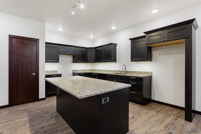 kitchen featuring light stone countertops, light wood-style floors, a sink, and a center island