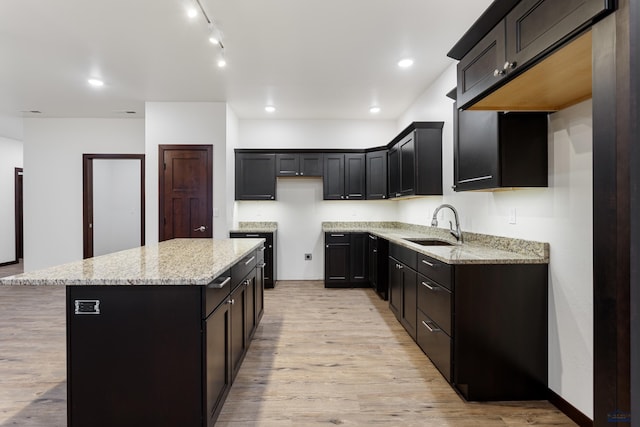 kitchen with light stone counters, recessed lighting, a sink, a kitchen island, and light wood finished floors