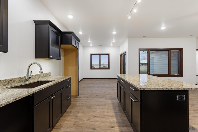 kitchen with recessed lighting, a sink, a kitchen island, light wood-style floors, and light stone countertops