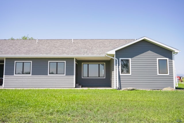 back of property with roof with shingles and a yard