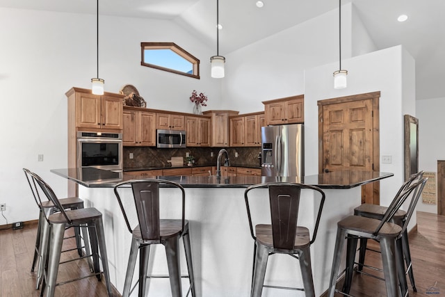 kitchen featuring dark hardwood / wood-style flooring, decorative backsplash, high vaulted ceiling, an island with sink, and appliances with stainless steel finishes