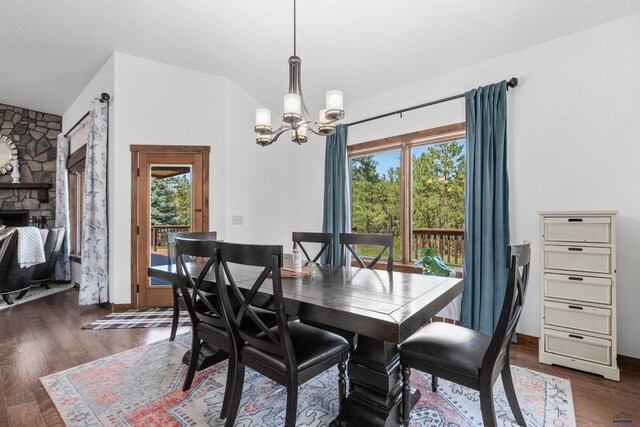 dining area featuring an inviting chandelier, a stone fireplace, and dark wood-type flooring