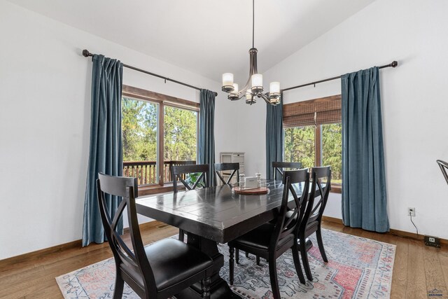 dining space featuring wood-type flooring, vaulted ceiling, a notable chandelier, and plenty of natural light