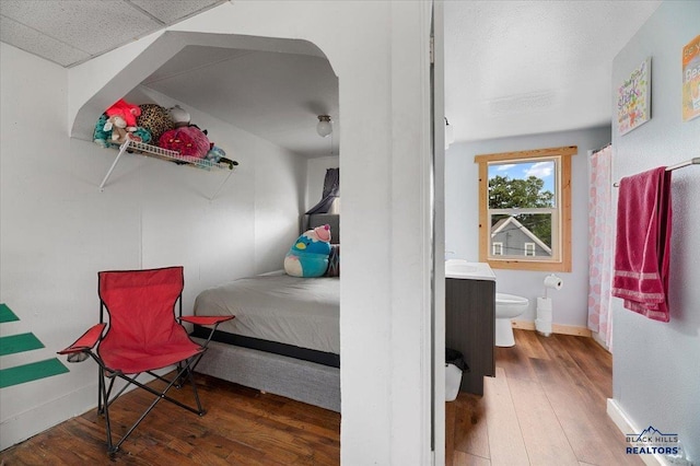 bedroom with a drop ceiling, hardwood / wood-style floors, and ensuite bath