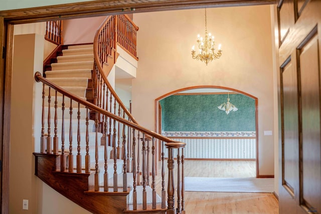 staircase featuring a towering ceiling, wood-type flooring, and a notable chandelier