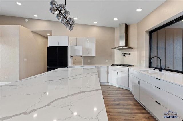 kitchen featuring gas stovetop, wall chimney range hood, white cabinets, wood finished floors, and a sink
