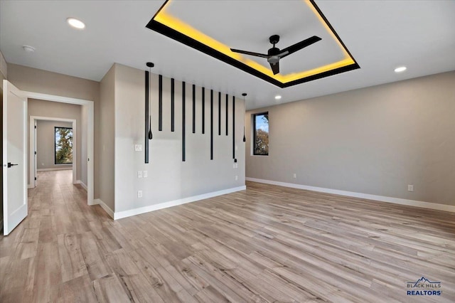 spare room featuring baseboards, a raised ceiling, ceiling fan, recessed lighting, and light wood finished floors