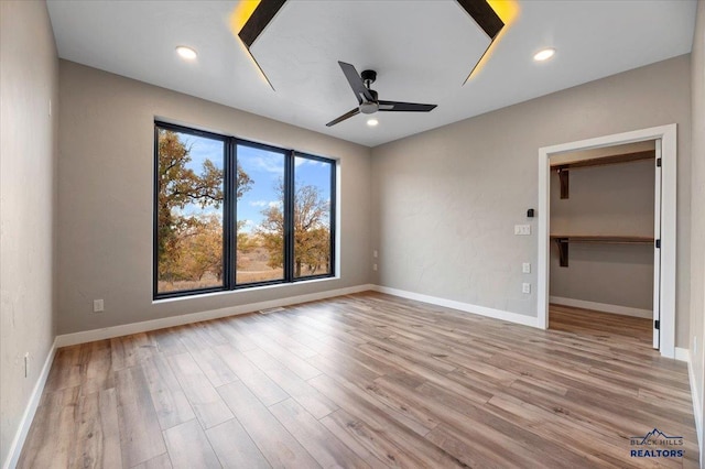 unfurnished bedroom featuring recessed lighting, baseboards, a walk in closet, and wood finished floors