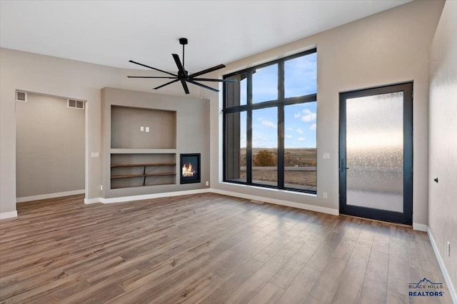 unfurnished living room featuring visible vents, built in features, baseboards, ceiling fan, and wood finished floors