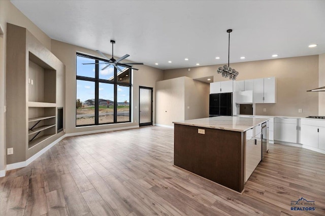 kitchen featuring white cabinets, a center island, baseboards, cooktop, and light wood-style floors