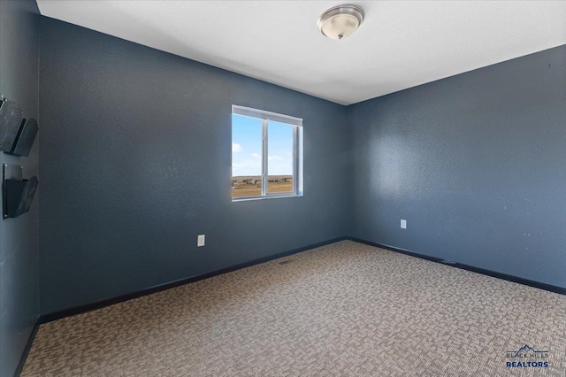 unfurnished room with a textured wall, carpet floors, and baseboards