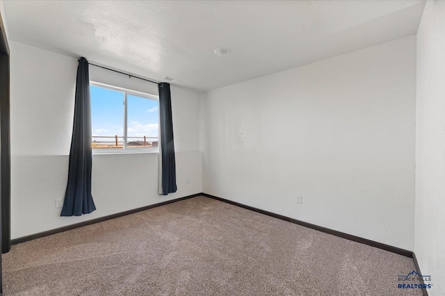 carpeted spare room with a textured ceiling and baseboards