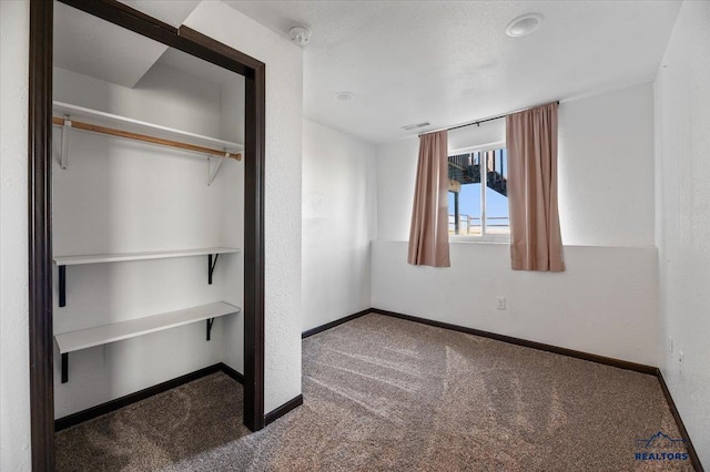 unfurnished bedroom with carpet, visible vents, baseboards, and a textured wall