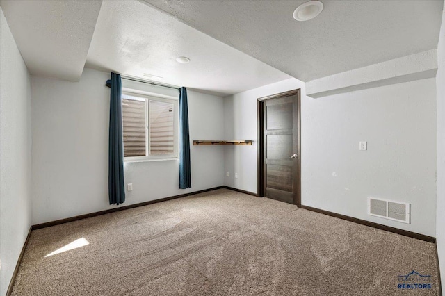 empty room featuring a textured ceiling, carpet, visible vents, and baseboards