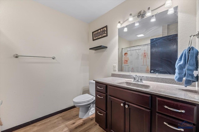 bathroom with curtained shower, toilet, vanity, wood finished floors, and baseboards