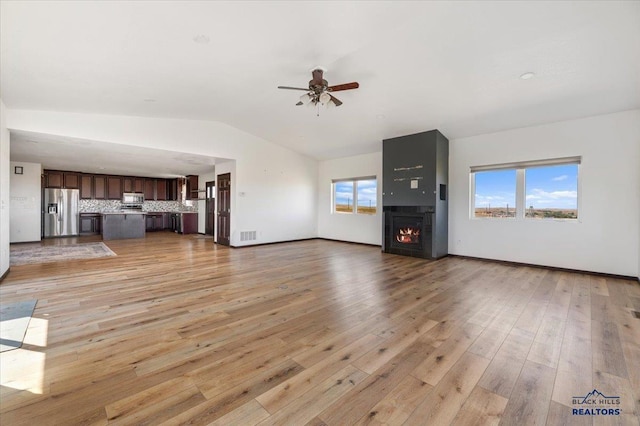 unfurnished living room with light wood-style floors, vaulted ceiling, ceiling fan, a lit fireplace, and baseboards