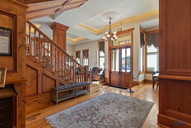 entryway with light hardwood / wood-style floors, decorative columns, crown molding, and an inviting chandelier