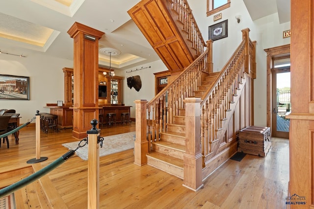 staircase with ornate columns, a raised ceiling, hardwood / wood-style flooring, and ornamental molding