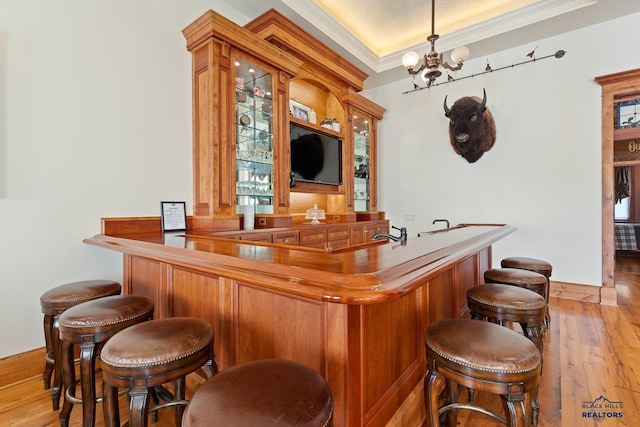 bar featuring a raised ceiling, crown molding, wood-type flooring, and an inviting chandelier