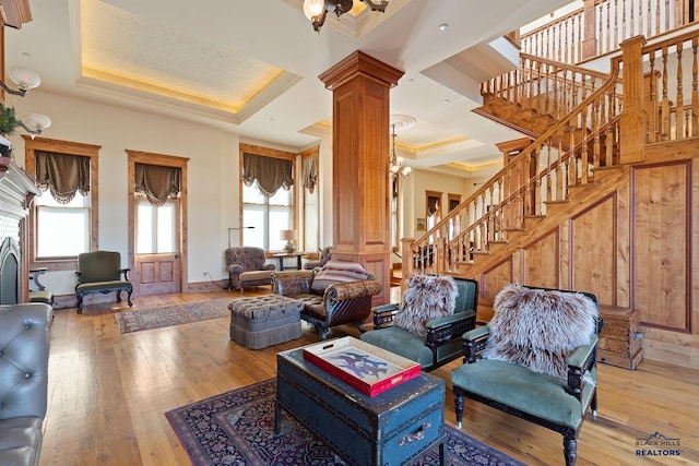 living room featuring wood-type flooring, a chandelier, coffered ceiling, a tray ceiling, and decorative columns