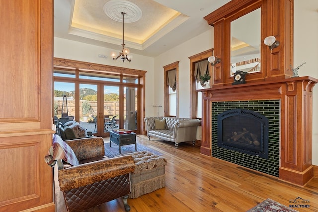 living room with a tray ceiling, an inviting chandelier, light wood-type flooring, and a tile fireplace