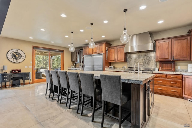 kitchen with light tile patterned flooring, wall chimney exhaust hood, light stone countertops, high end fridge, and a large island