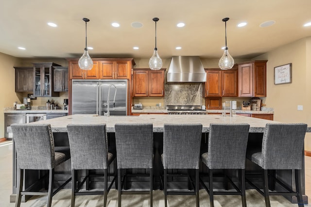 kitchen featuring decorative backsplash, a spacious island, high end fridge, wall chimney range hood, and stove