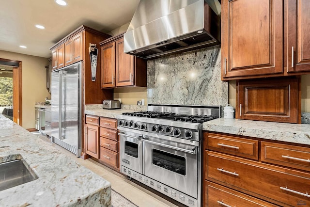 kitchen with wall chimney range hood, light stone counters, and high quality appliances