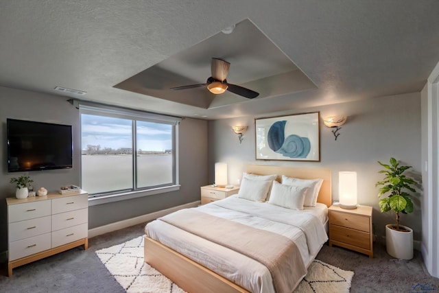 carpeted bedroom with ceiling fan, a raised ceiling, and a textured ceiling