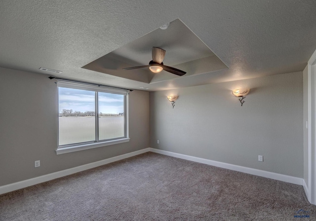 spare room featuring a textured ceiling, carpet flooring, ceiling fan, and a raised ceiling