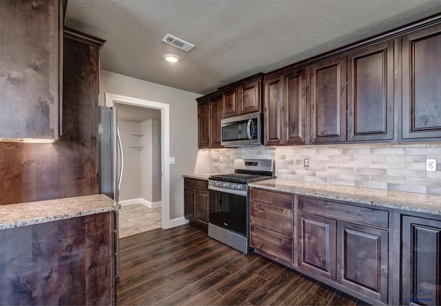 kitchen with dark hardwood / wood-style floors, tasteful backsplash, appliances with stainless steel finishes, light stone counters, and a textured ceiling